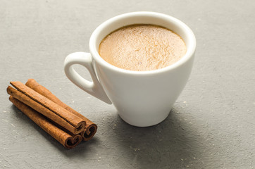 a cup of coffee and cinnamon stick on a grey background