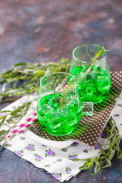 Drink from an estragon with ice in a glass on a table. Selective focus. Copy space
