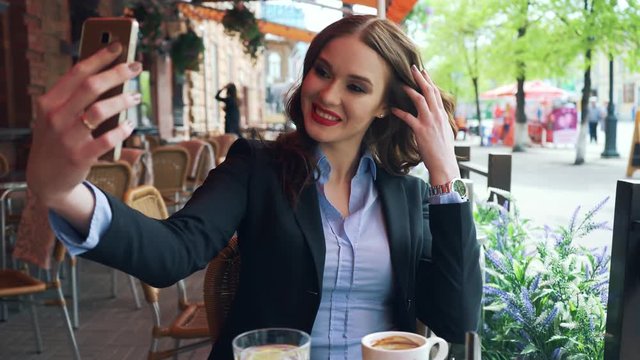 A luxurious young girl in a business suit makes herself selfie in a cafe.