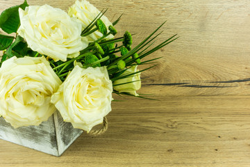 White roses with green leaves on a rustic wooden table