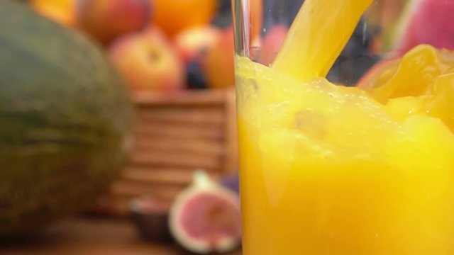 Orange juice is poured into a glass on a background of a still-life of fresh fruit on a wooden table