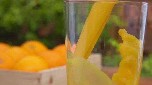 Orange juice is poured into a glass on a background of a box of ripe oranges. close-up camera motion