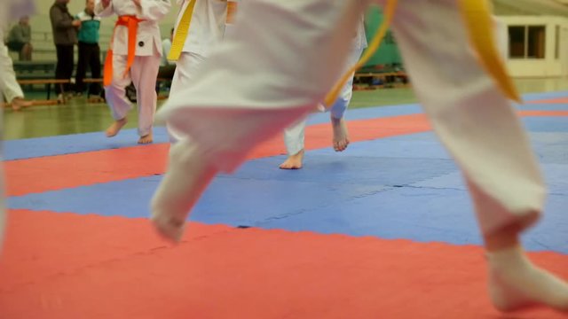 Group of karateka teenagers in kimono runs on tatami in the gym