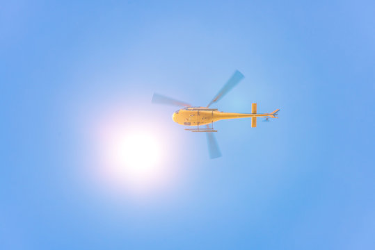 Yellow helicopter from below against blue sky with sun