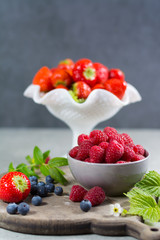 Fresh organic summer berries - ripe raspberry, strawberry, blueberry with leaves on wood background