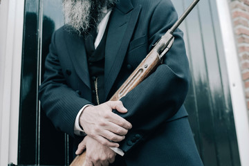 Hands of man holding rifle while leaning against window shutters.