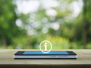 Information sign icon on modern smart phone screen on wooden table over blur green tree in park,...