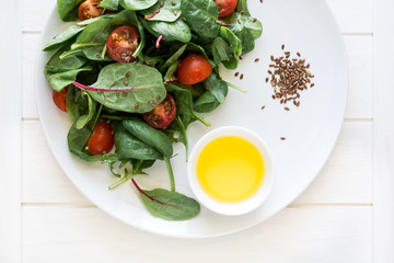 Fresh spring vegetarian salad with lettuce mix, cherry tomatoes, olive oil and flax seeds on white plate. Selective focus