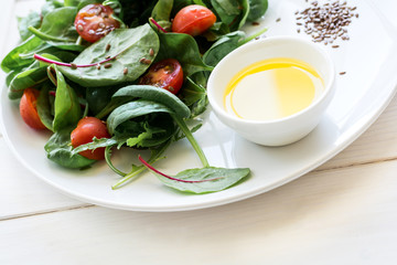 Fresh spring vegetarian salad with lettuce mix, cherry tomatoes, olive oil and flax seeds on white plate. Selective focus