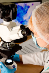 Laboratory assistant or technician in medical research lab looking into a microscope and doing research