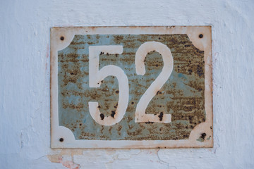 Very old rusty house number 52 plate on cracked white facade