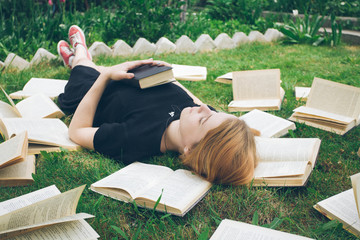 Young girl reading a book while lying in the grass. A girl among the books in the summer garden