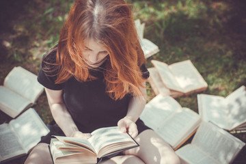 Obraz premium Young girl reading a book while lying in the grass. A girl among the books in the summer garden