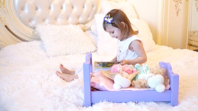 An active little preschool child, a pretty little girl with a blond curly hair, plays with her dolls, puts them to sleep in
