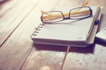 Notebook or note pad,smart phone,cup of coffee and glasses on wooden background with copy space. office desk concept