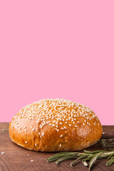 Burger bun with sesame seeds on pink background. Copy space for text