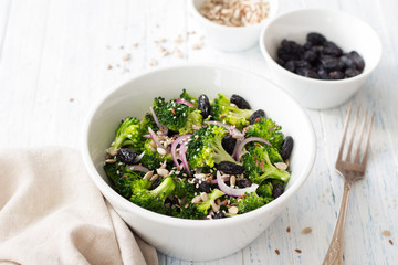 Broccoli with raisins, red onions and seeds. Healthy raw diet salad. In a white bowl on a blue wooden background. Selective focus