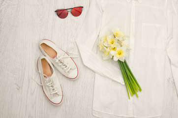 White shirt, glasses, sneakers and a bouquet of daffodils. Wooden background. Fashionable concept
