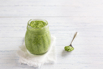Fresh homemade pesto sauce from arugula with pine nuts in a glass jar on a blue wooden background. Delicious healthy food. Selective focus