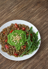 Homemade lentils with tomatoes and pesto sauce from arugula on a wooden background. Delicious healthy food