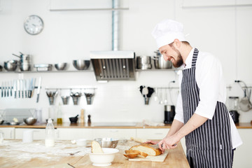 Young pastry-chef slicing bread at workplace