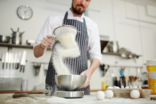 Baker sifting flour for dough through bolter
