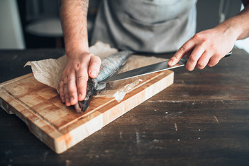 Chef hands with knife cut up fish on cutting board