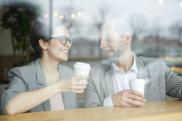 Two happy colleagues with hot drinks interacting at break