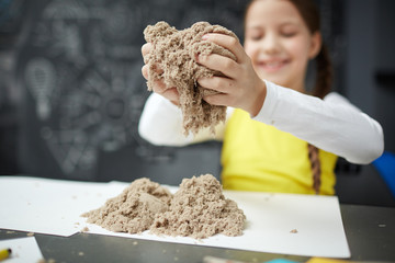 Portrait of cute little girl enjoying play with kinetic sand in daycare center, smiling happily