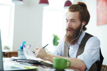 Portrait of trendy bearded man video chatting with business partners working in modern office