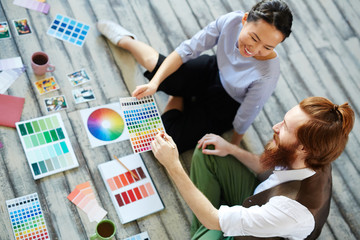 High angle view of creative designers team working in modern studio sitting on wooden floor and  discussing projects color scheme, smiling cheerfully