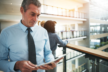 Adult pensive office worker standing and using tablet