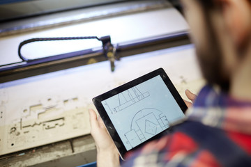 High angle shot of factory worker using digital tablet to operate laser cutting machine in workshop