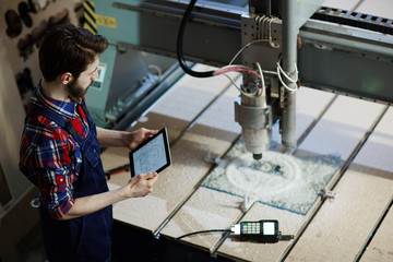 Factory worker operating cutter machine using digital tablet in workshop