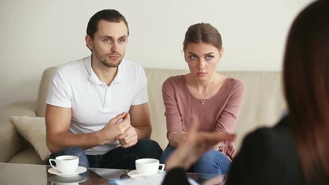 Family facing relationship difficulties. Young upset couple visiting professional psychotherapist office, listening to marriage counselor advice, looking at each other, making up after therapy session