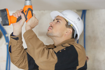 young man drilling a hole in white ceiling