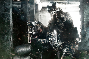 Two heavily armed masked paintball soldier on post apocalyptic background. Ad concept.