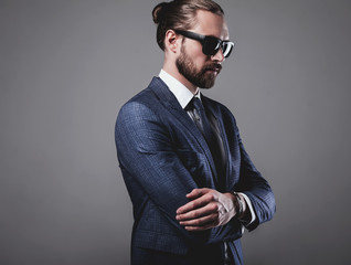 portrait of handsome fashion businessman  model dressed in elegant blue suit with sunglasses.posing on gray background in studio