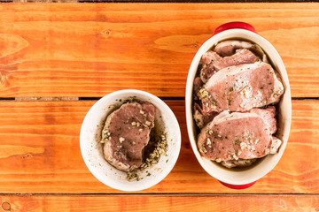 Flat lay top view marinated raw pork chops above wooden table.