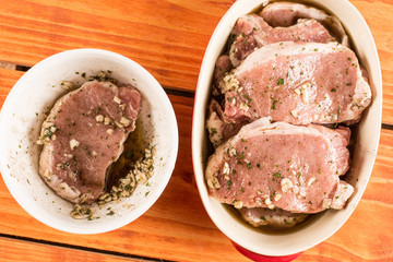 Flat lay top view marinated raw pork chops above wooden table.