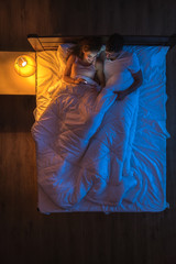 The happy couple with a phone lay on a bed. Evening night time. View from above