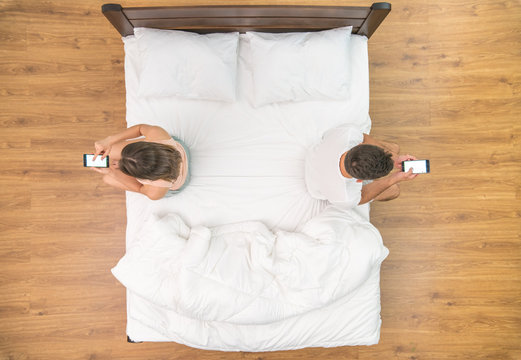 The man and woman with phone sit on the bed. view from above