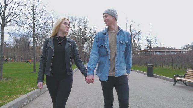 Young beautiful couple, blond and her boyfriend are walking in the park, holding hands. Go to the camera. A beautiful sunny day.