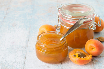 

 Freshly cooked dessert. Ripe apricots and two jars of jam on a light wooden background.