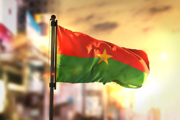 Burkina Faso Flag Against City Blurred Background At Sunrise Backlight