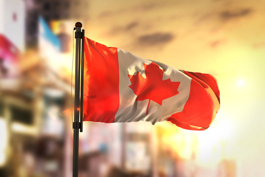 Canada Flag Against City Blurred Background At Sunrise Backlight