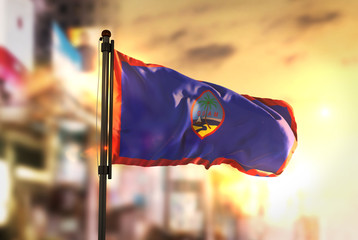 Guam Flag Against City Blurred Background At Sunrise Backlight