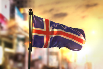 Iceland Flag Against City Blurred Background At Sunrise Backlight