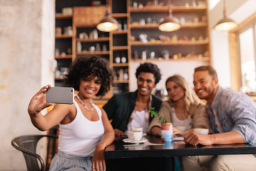 Multiracial friends taking selfie on smart phone at cafe