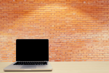 blank screen laptop on wooden table with retro red brick wall blurred background